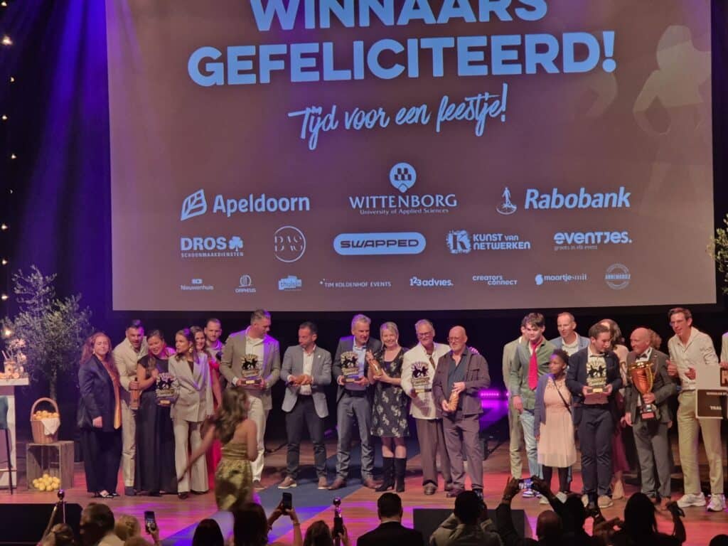 Alle winnaars op het podium onder het scherm Winnaars gefeliciteerd